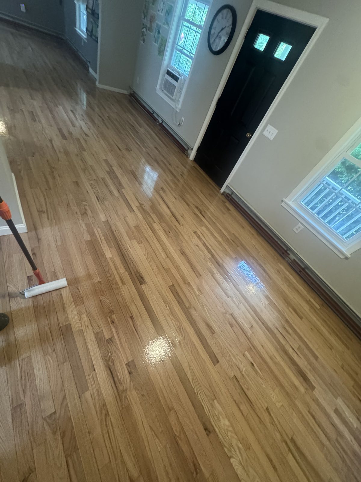 Applying professional water-based polyurethane finish to a hardwood floor in Coventry, Rhode Island — applicator laying down a fresh coat with wet glossy streaks across the bare wood